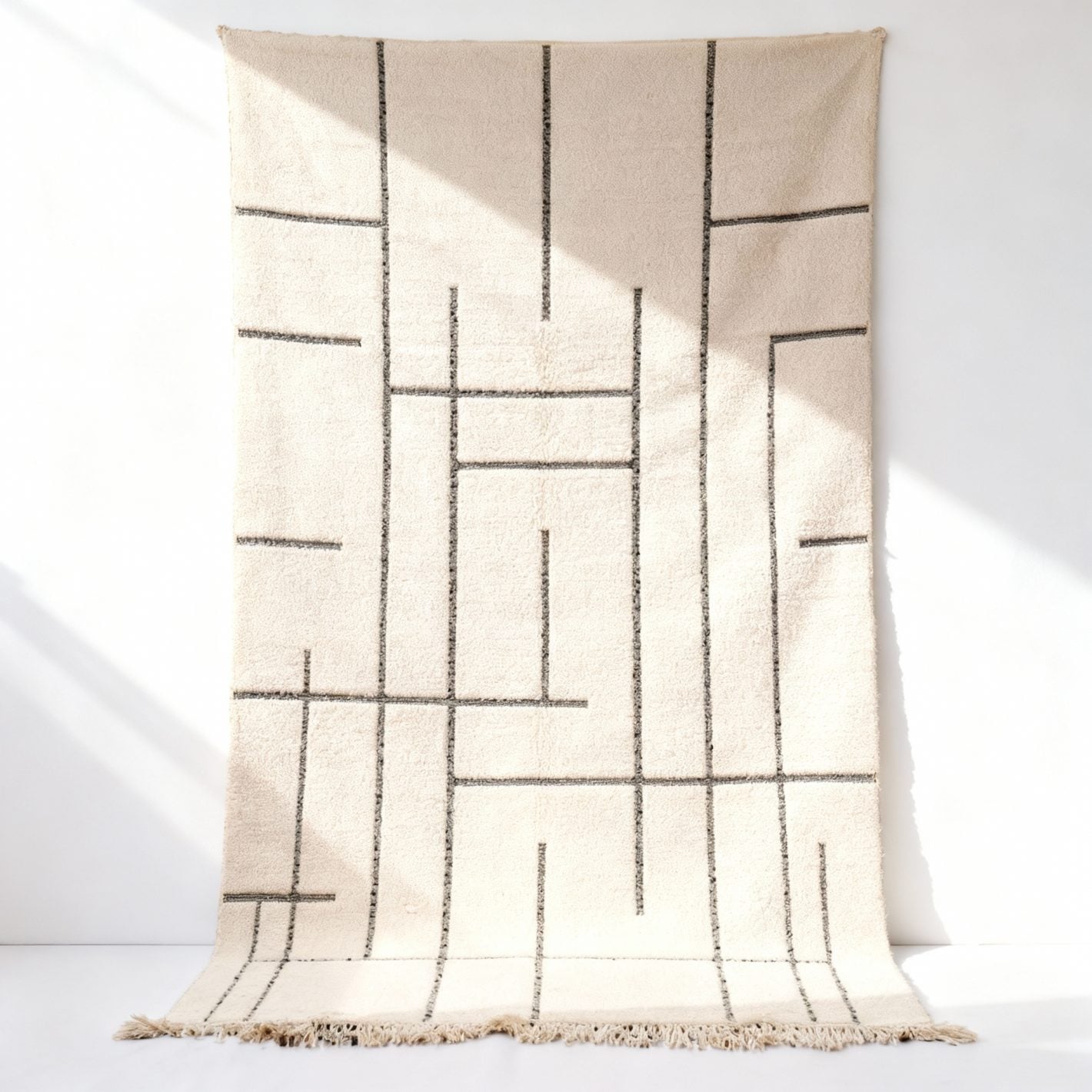 Handmade white Moroccan geometric rug hanging in studio with charcoal Berber lines and wool texture Handmade white Moroccan geometric rug hanging in studio with charcoal Berber lines and wool texture