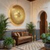 Brass filigree wall lamp illuminated in traditional Moroccan riad with zellige tiles creating ornate shadow patterns