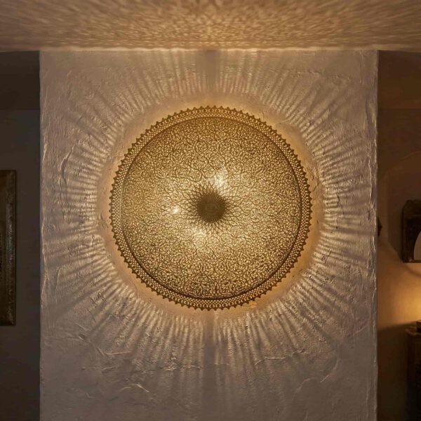 Brass filigree wall lamp mounted on textured white wall projecting warm geometric light patterns
