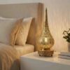 Teardrop brass accent lamp glowing warmly on modern nightstand with stacked books and small plant in neutral bedroom Teardrop brass accent lamp glowing warmly on modern nightstand with stacked books and small plant in neutral bedroom