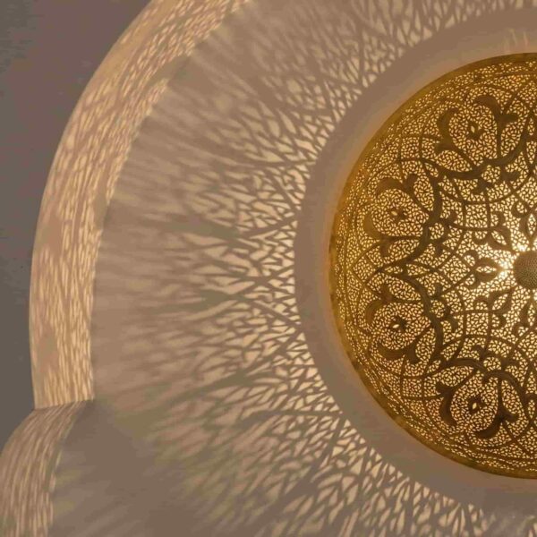 Brass wall sconce projecting dramatic sunburst shadow pattern on ceiling showing detailed light rays from perforated arabesque design