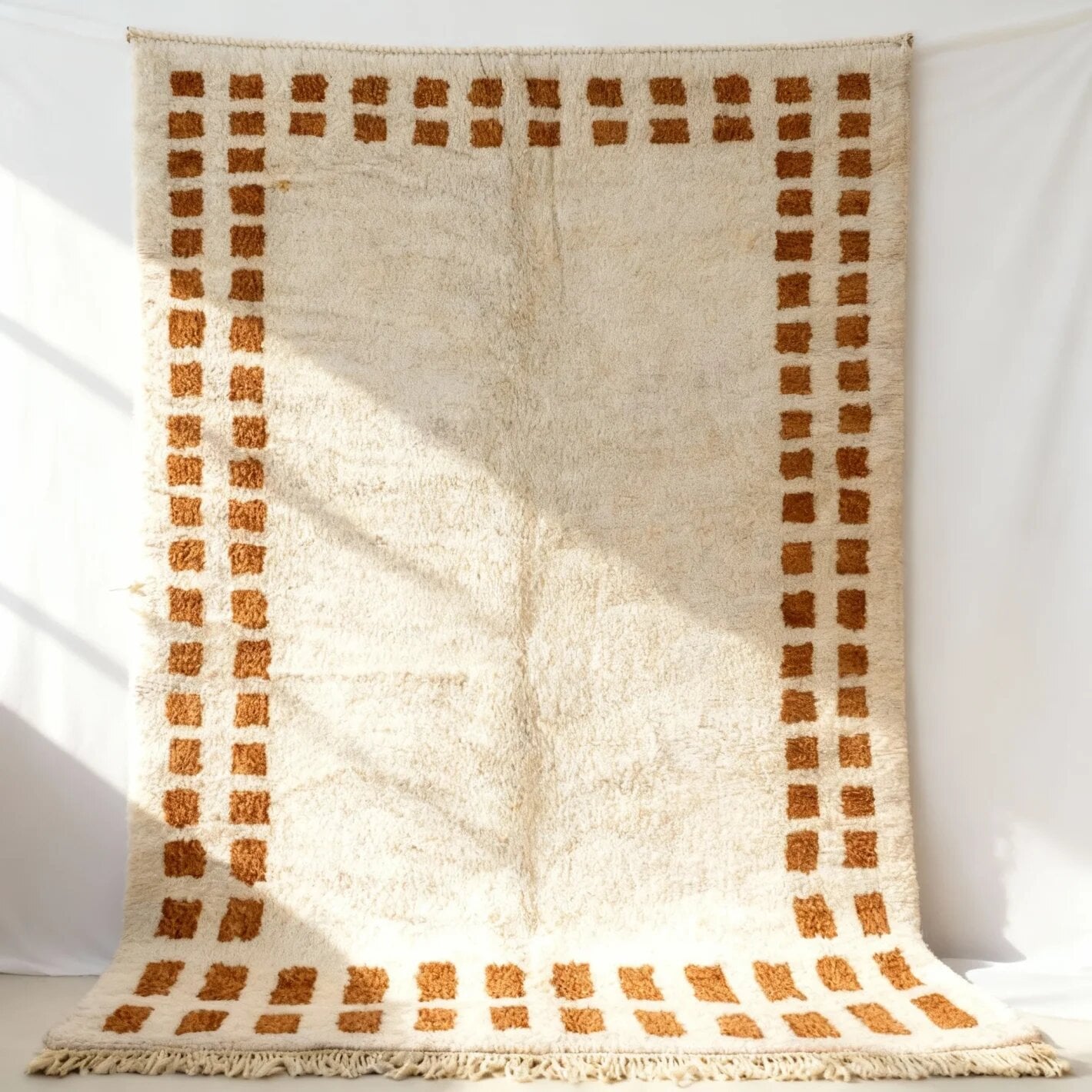Terracotta border wool rug with geometric Berber pattern, cream high-pile texture, and fringe detail against white wall