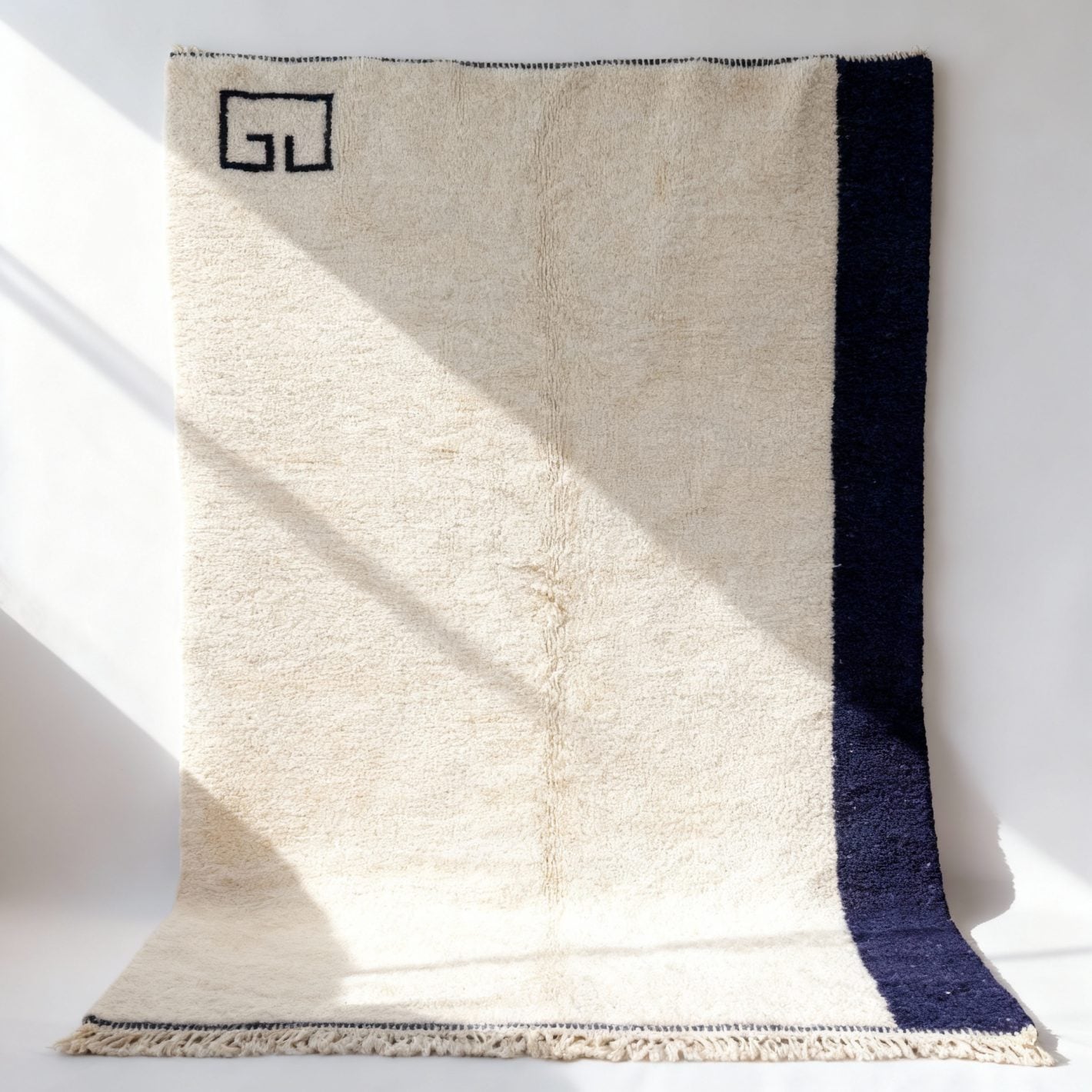 Minimalist navy wool rug with cream high-pile texture, Greek key border, and corner detail on white background Minimalist navy wool rug with cream high-pile texture, Greek key border, and corner detail on white background