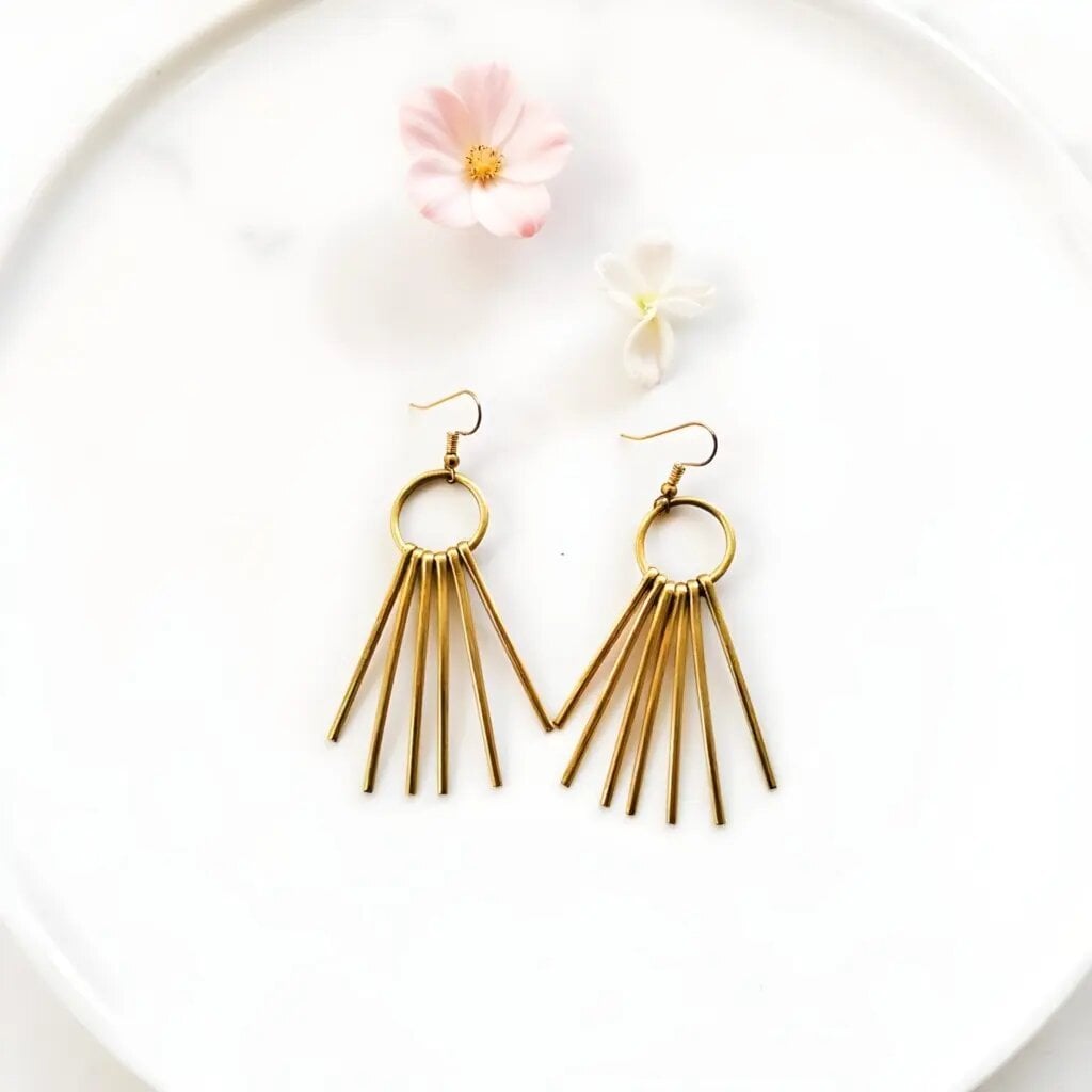 Handmade brass fringe earrings with gold sunburst design featuring metal spike drops on white ceramic plate Handmade brass fringe earrings with gold sunburst design featuring metal spike drops on white ceramic plate