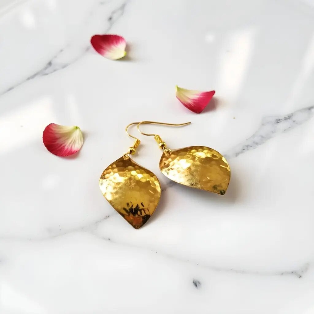 Handmade hammered brass earrings with golden leaf design on marble surface with rose petals
