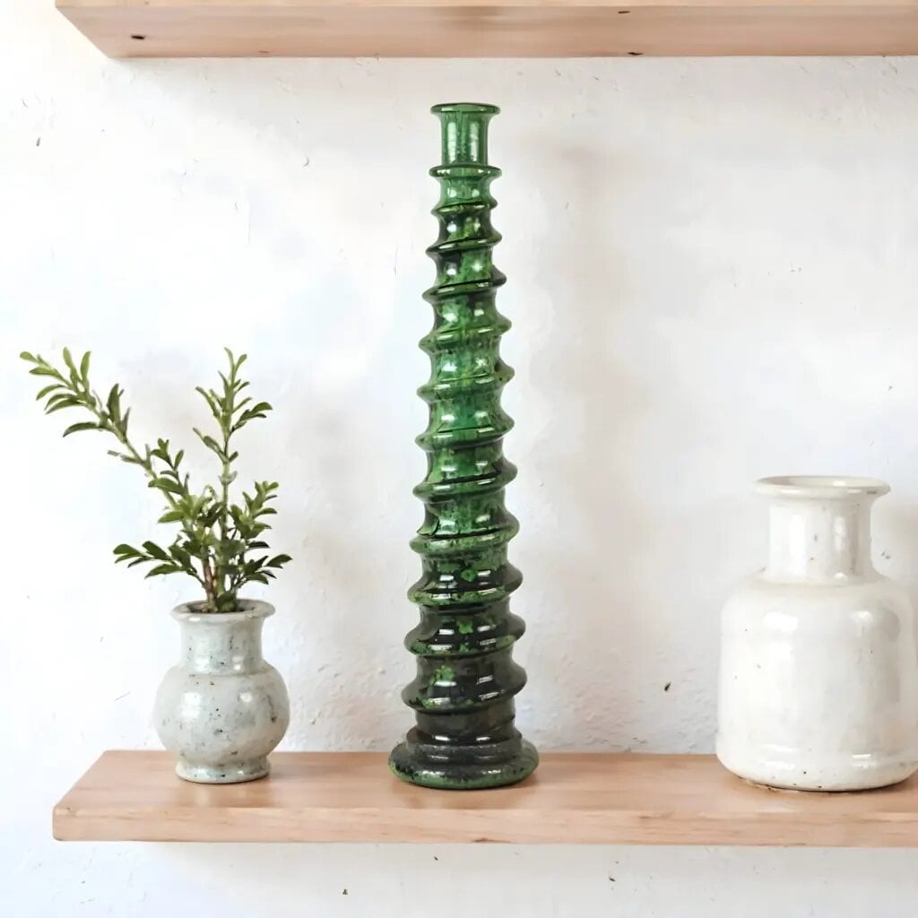Green glazed ceramic candle holder with spiral tower design on wooden shelf with plants Green glazed ceramic candle holder with spiral tower design on wooden shelf with plants