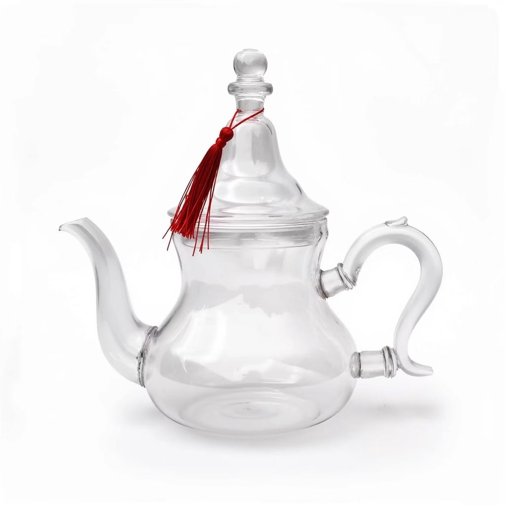 Handblown borosilicate glass teapot with crimson silk tassel and gooseneck spout on white background Handblown borosilicate glass teapot with crimson silk tassel and gooseneck spout on white background