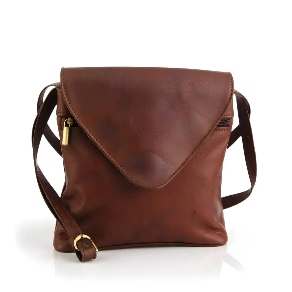 Brown leather envelope crossbody purse displayed on wooden shelf with woven basket and pottery decor