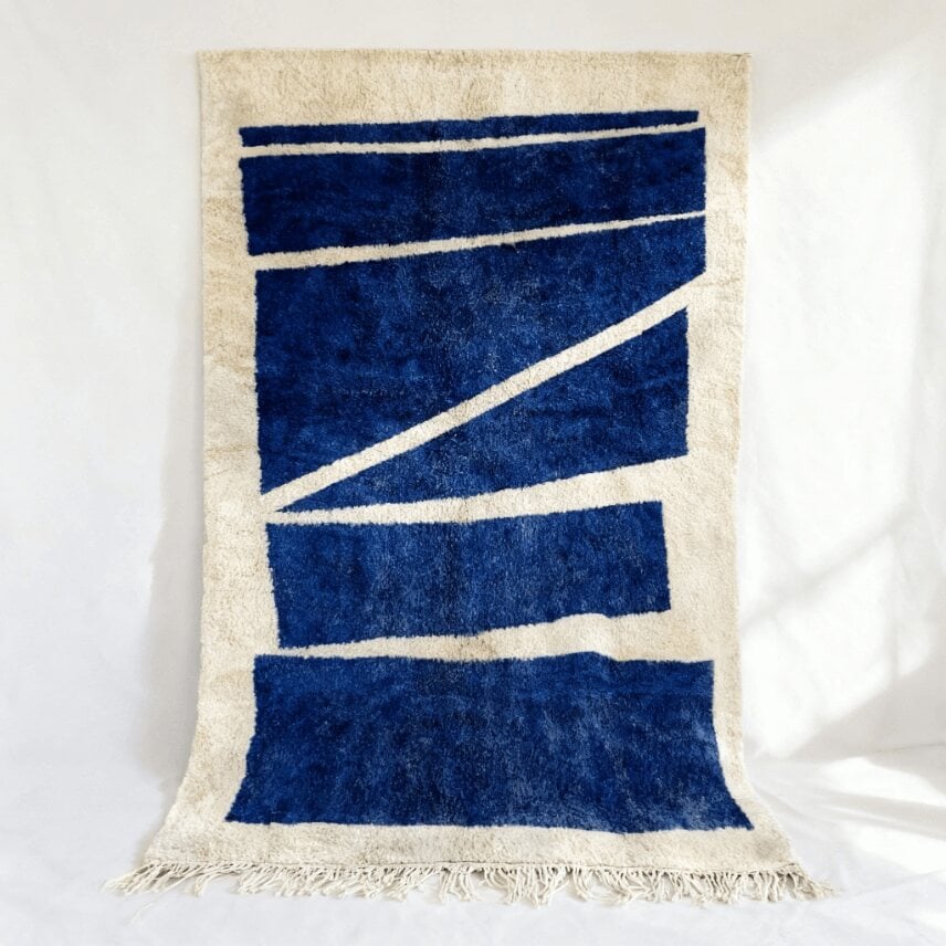 Navy blue Moroccan Beni rug with geometric pattern and cream wool fringe hung against white wall