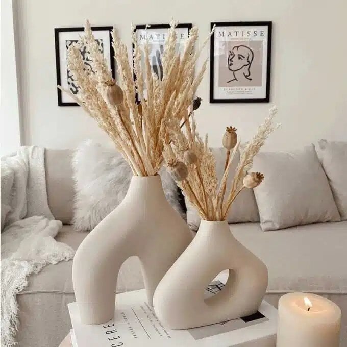 Beige matte ceramic vase set of 2 with sculptural cutouts holding dried pampas and poppy stems on coffee table