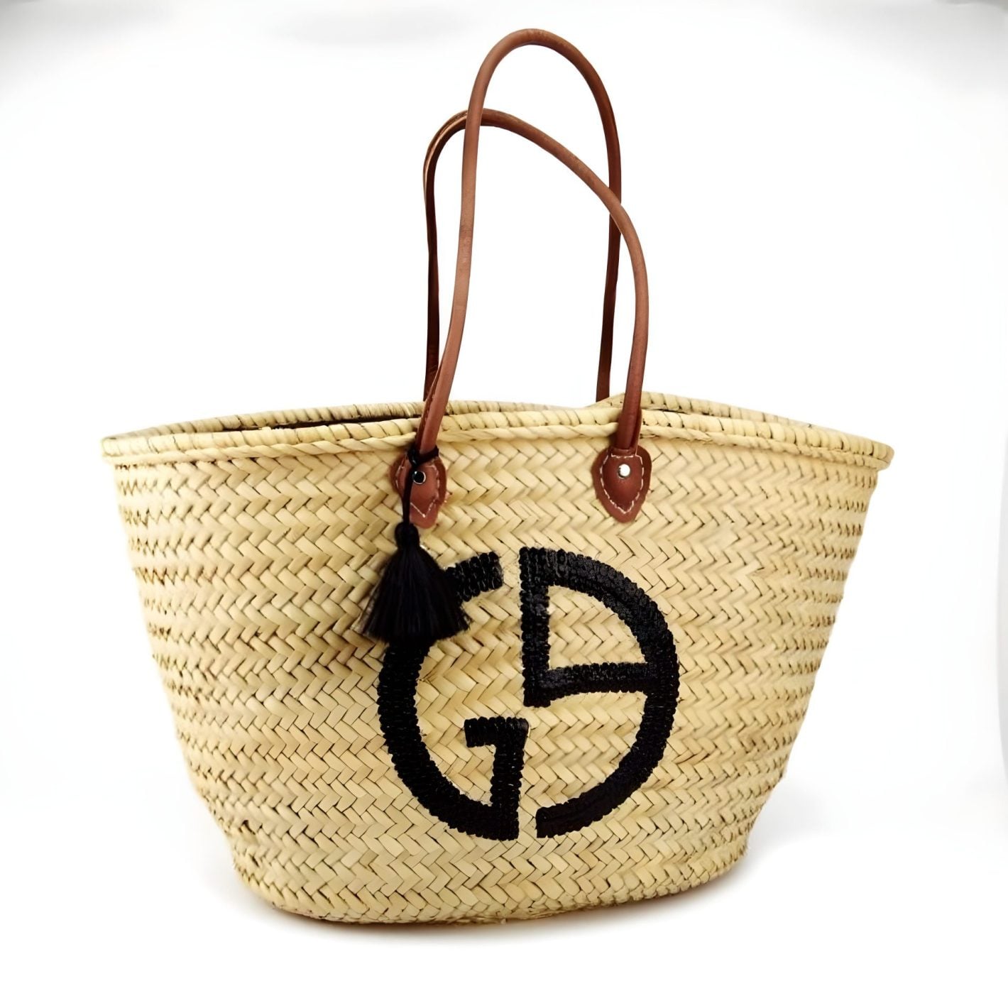Handwoven straw bag with black GD monogram and brown leather handles on white background