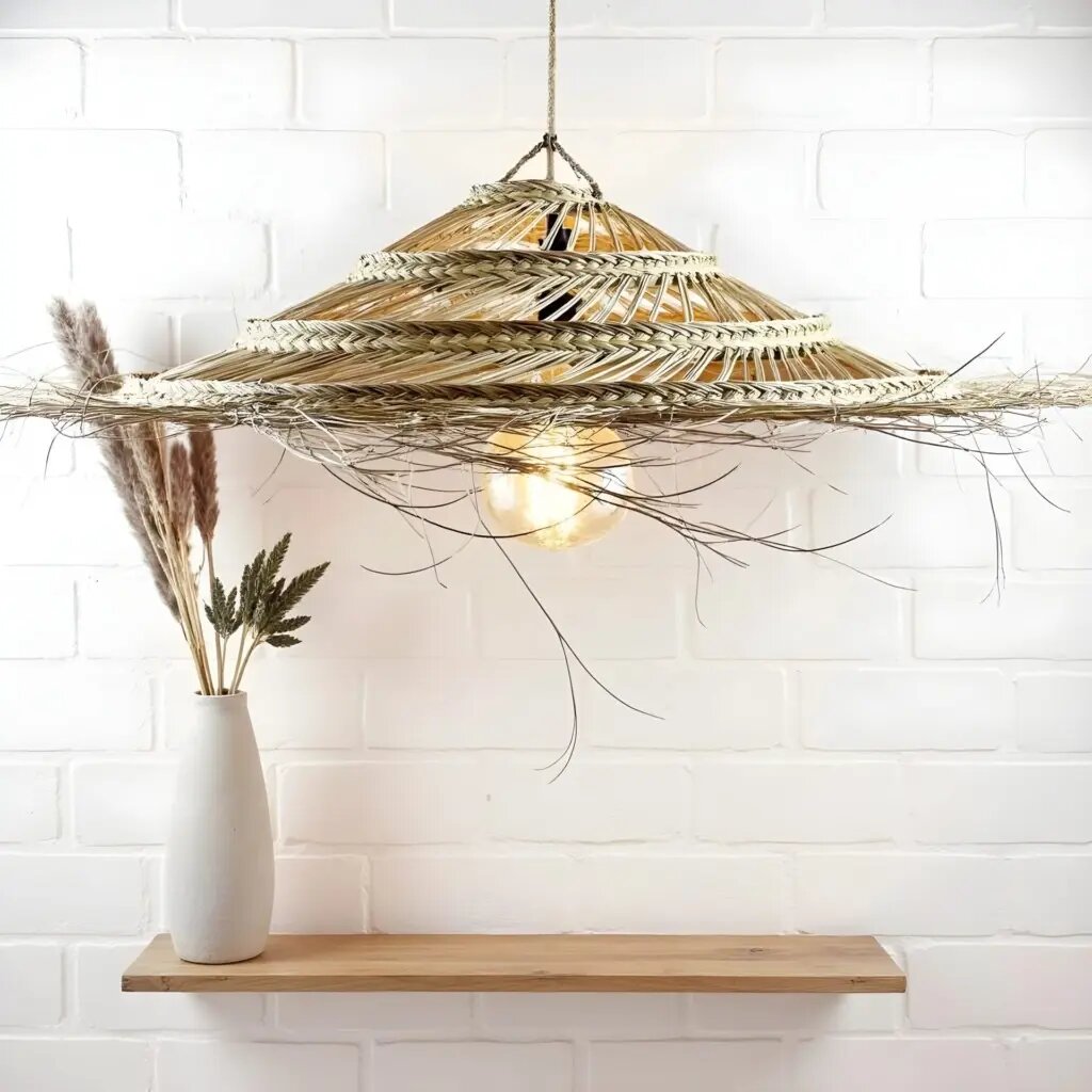 Handwoven palm leaf pendant light with three tiers and frayed edges against white brick wall, creating warm ambiance Handwoven palm leaf pendant light with three tiers and frayed edges against white brick wall, creating warm ambiance