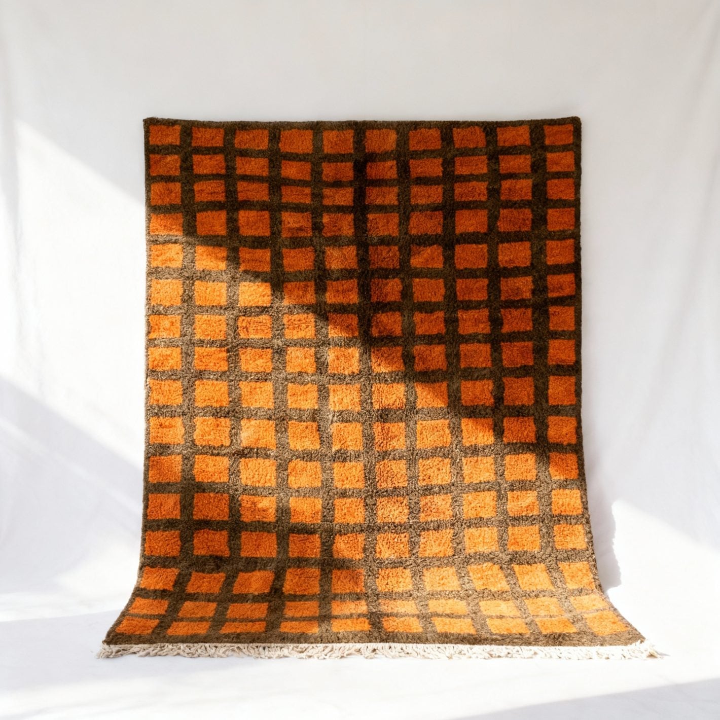 Handmade Moroccan trellis rug with orange squares on brown grid, displayed on white wall