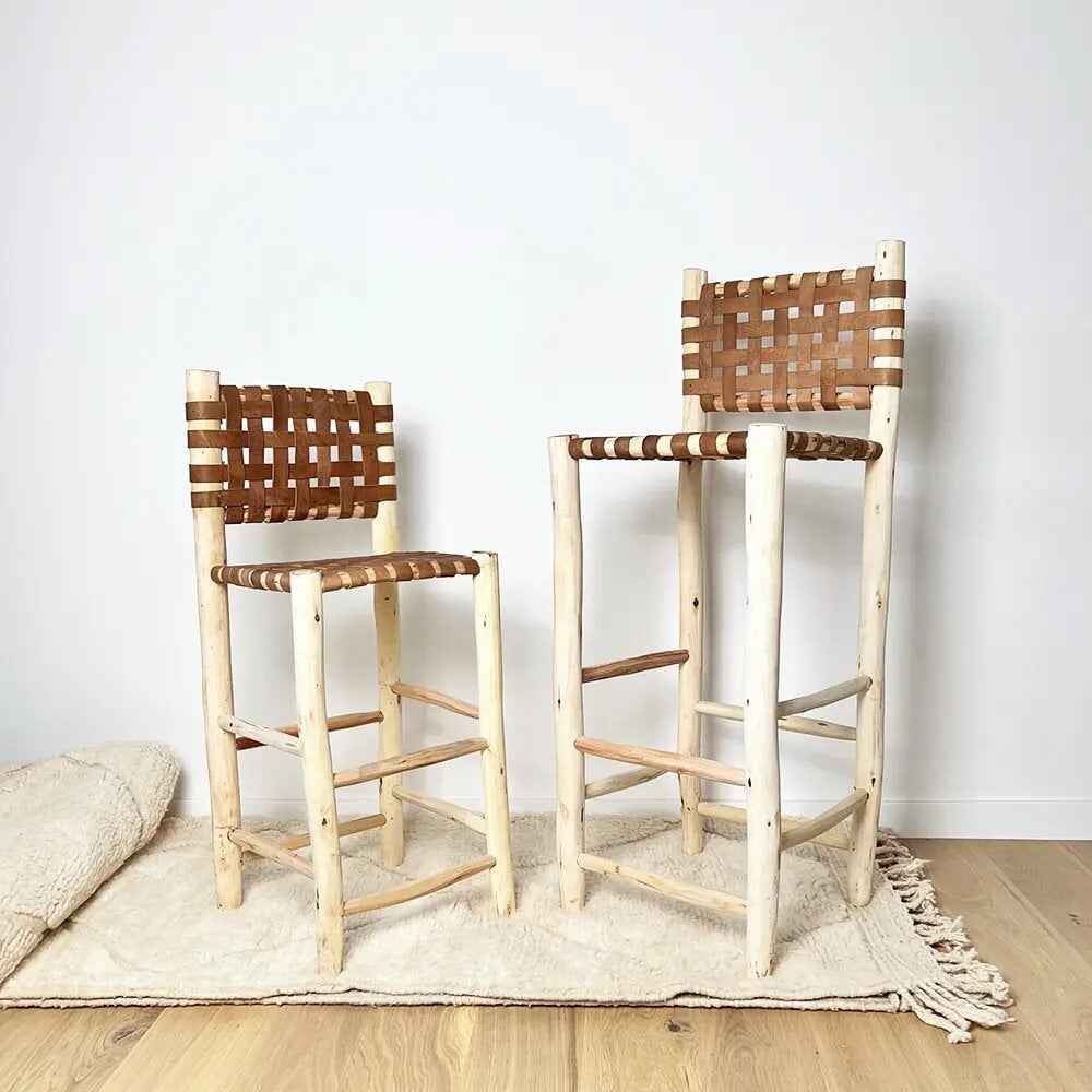 Handwoven leather bar stool pair with natural wood frame and brown woven cowhide seats on cream rug Handwoven leather bar stool pair with natural wood frame and brown woven cowhide seats on cream rug