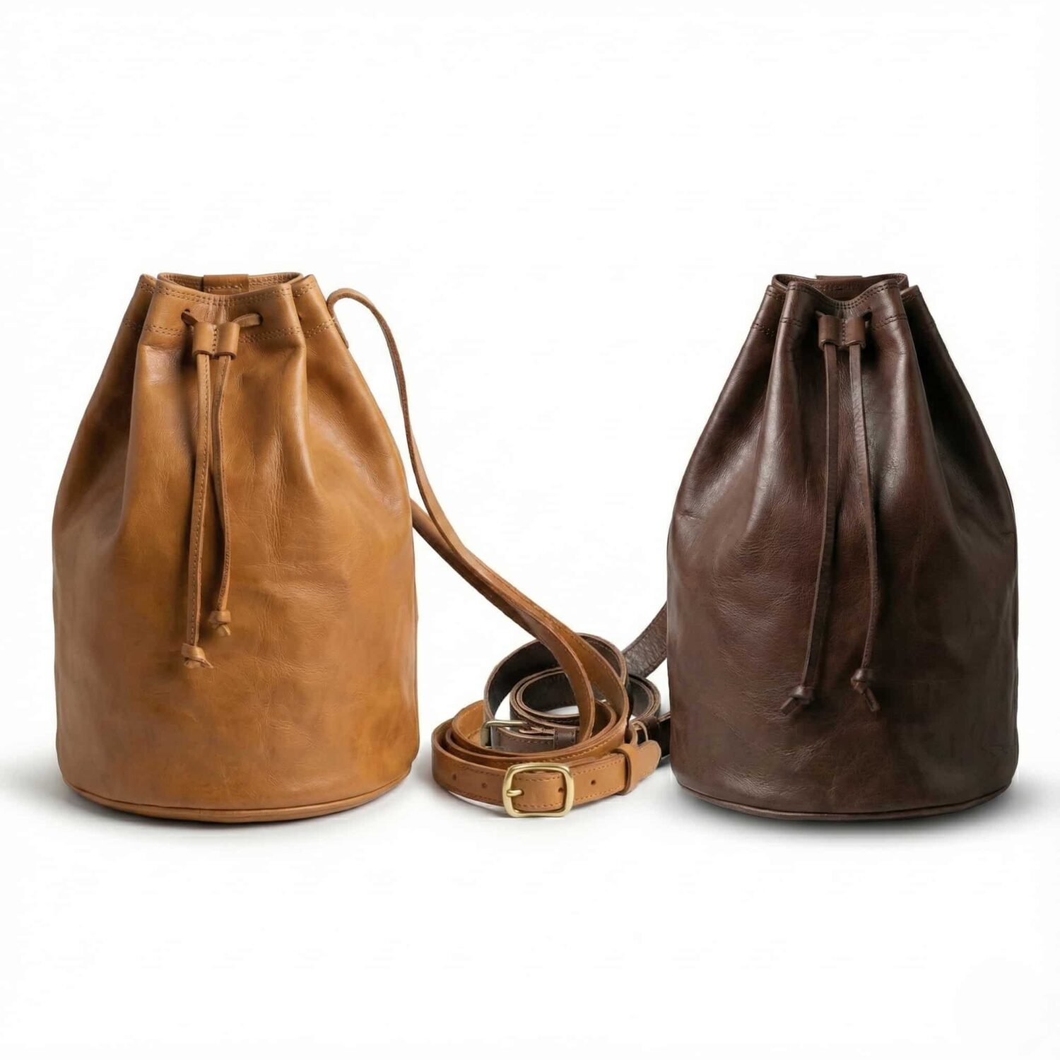 Tan and dark brown leather bucket bags with drawstring closures and adjustable crossbody straps on white background Tan and dark brown leather bucket bags with drawstring closures and adjustable crossbody straps on white background