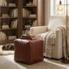 Channel stitched leather cube ottoman serving as a side table with books and a mug in a cozy reading nook Channel stitched leather cube ottoman serving as a side table with books and a mug in a cozy reading nook
