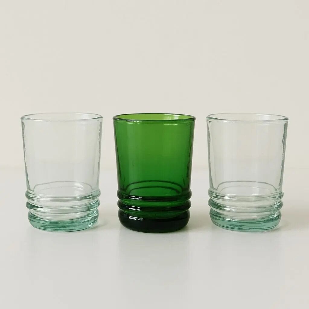 Recycled glass tumblers in emerald green and clear showing hand-blown ribbed bases in a three-glass lineup Recycled glass tumblers in emerald green and clear showing hand-blown ribbed bases in a three-glass lineup