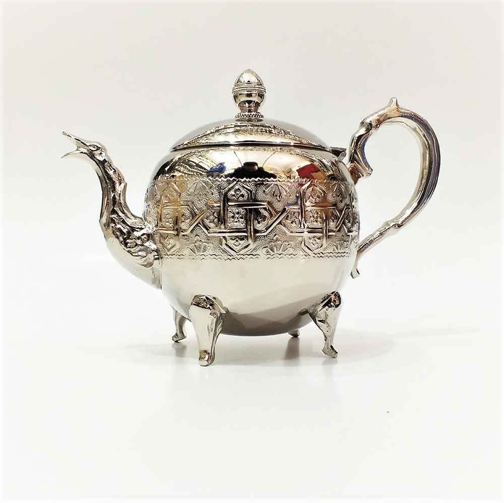 Grand round engraved silver teapot with footed base, hinged lid, and geometric medallion band on plain off-white backgro Grand round engraved silver teapot with footed base, hinged lid, and geometric medallion band on plain off-white background