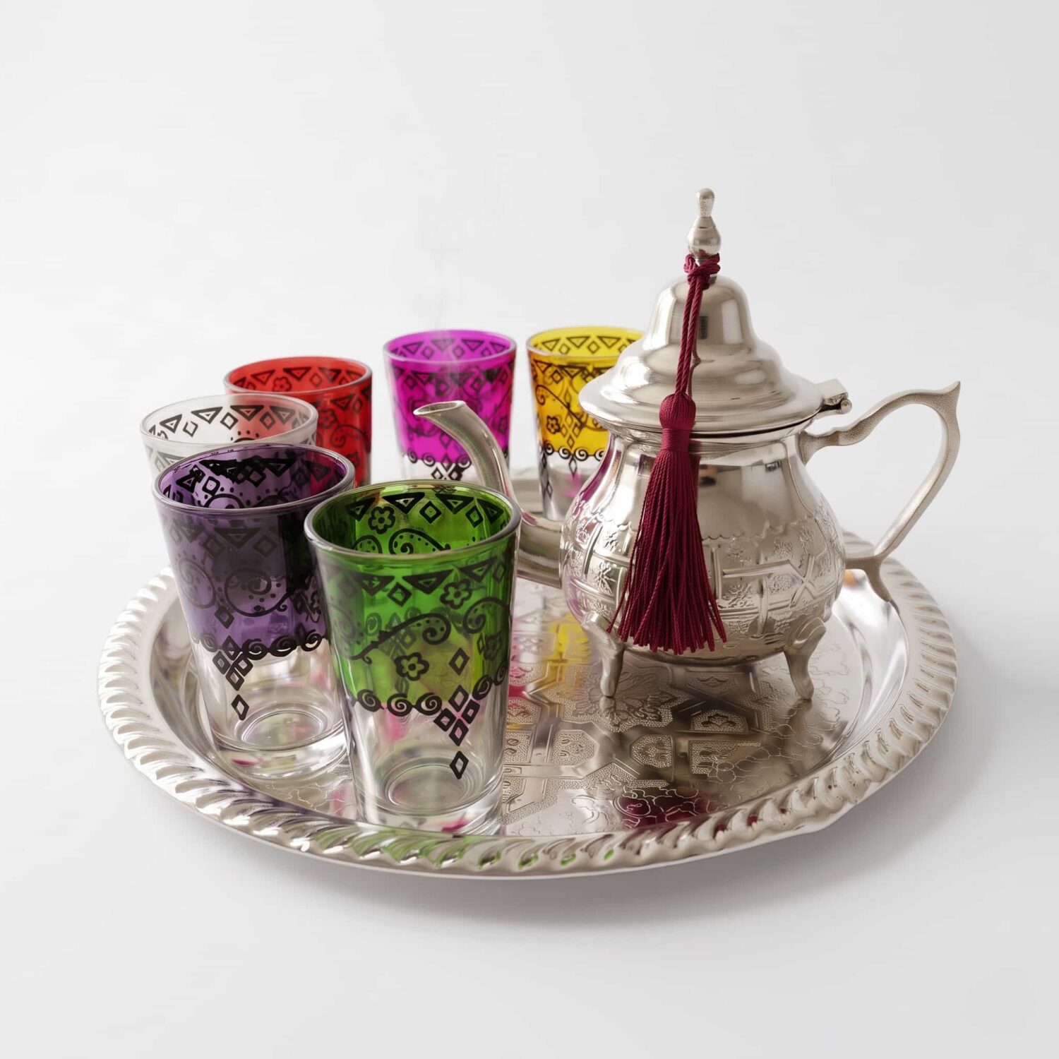 A vibrant hand-engraved silver tea set multicolor glasses featuring a detailed teapot adorned with a red tassel and six A vibrant hand-engraved silver tea set multicolor glasses featuring a detailed teapot adorned with a red tassel and six brightly colored tea glasses with black geometric designs, a