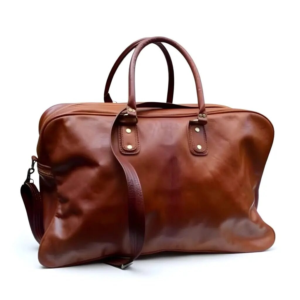 Handcrafted cognac leather weekend bag with double handles, solid brass rivets, and detachable strap on white background