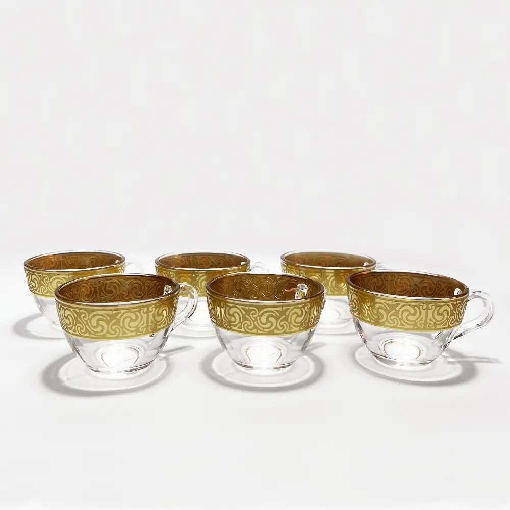 Gold hand-painted geometric scrollwork on clear glass coffee cups with integrated saucer seen from above Gold hand-painted geometric scrollwork on clear glass coffee cups with integrated saucer seen from above