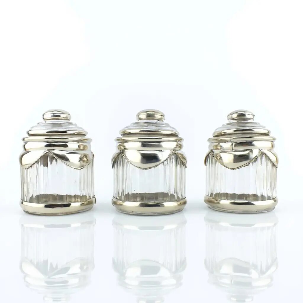 Three glass spice jars with silver-plated trim and ribbed design, featuring dome lids and decorative swag details Three glass spice jars with silver-plated trim and ribbed design, featuring dome lids and decorative swag details