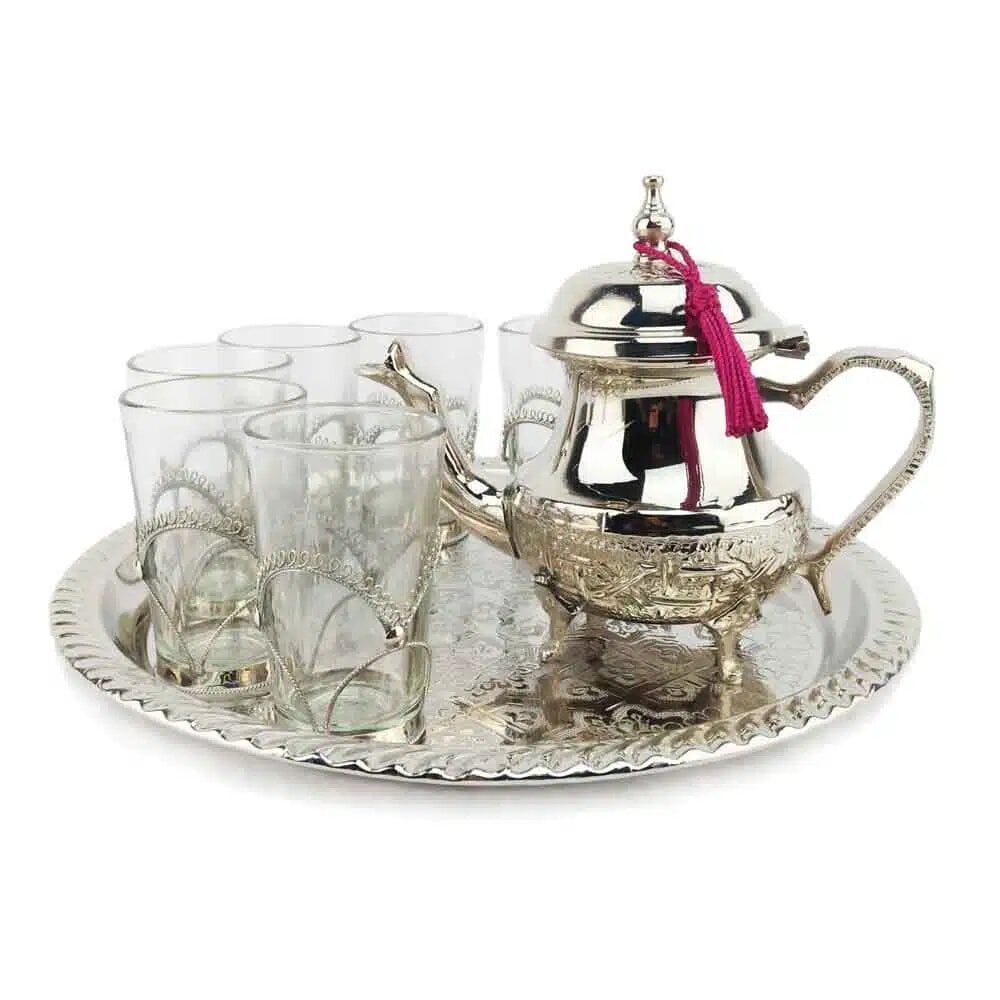 Eight-piece silver tea gift set with engraved teapot, pink tassel, six filigree glasses, and round tray on white backgro Eight-piece silver tea gift set with engraved teapot, pink tassel, six filigree glasses, and round tray on white background