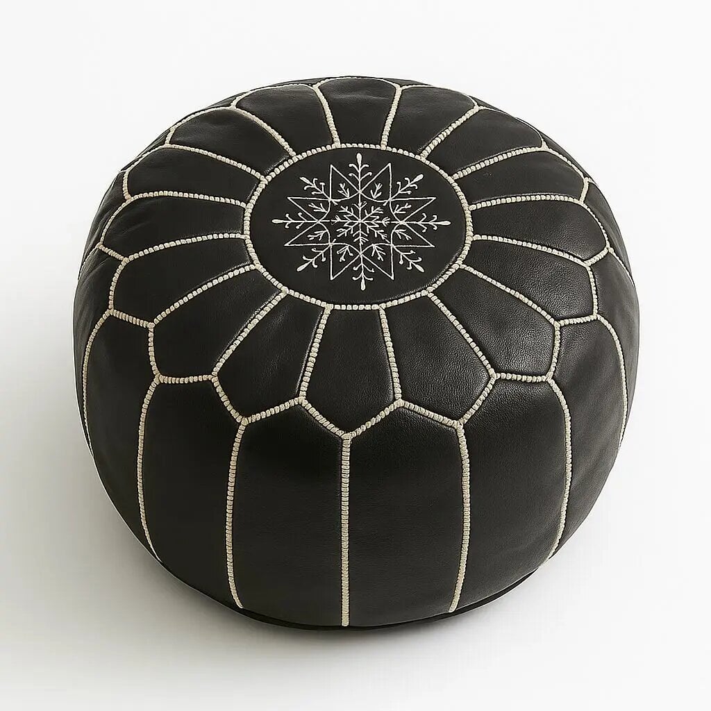 Round black leather floor ottoman with white geometric hand stitching and central medallion on plain background