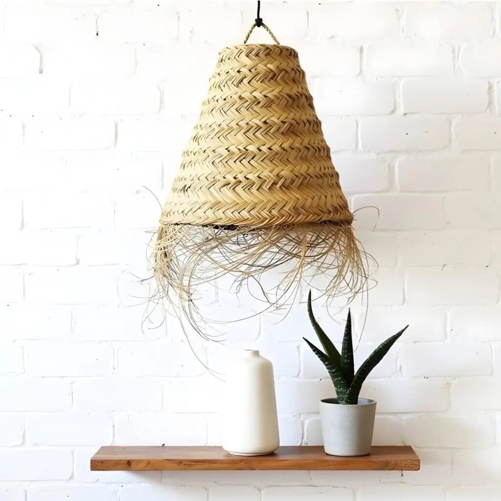 Handwoven straw pendant light with chevron weave pattern and natural fringe trim over white brick wall Handwoven straw pendant light with chevron weave pattern and natural fringe trim over white brick wall