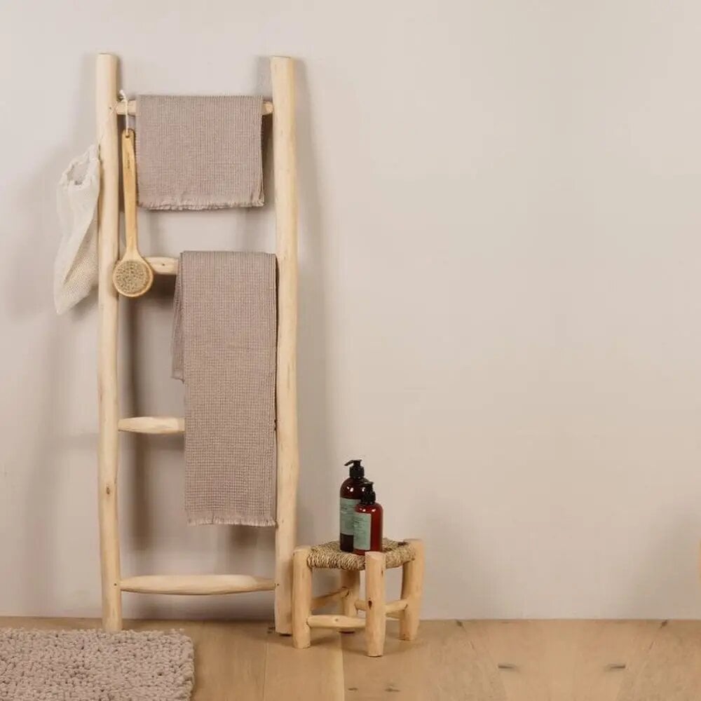 Natural lemon wood towel ladder with beige towels, brush, and small stool in minimalist bathroom setting