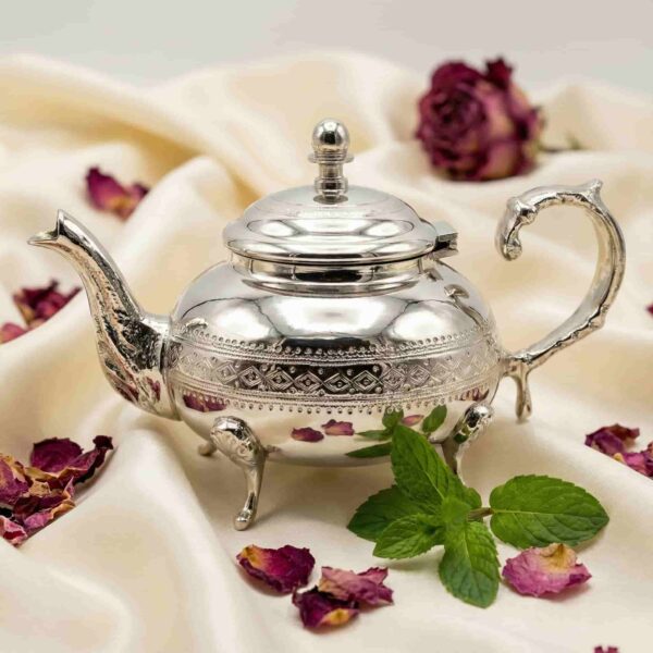 Silver teapot with hand-engraved diamond pattern displayed beside pink flowers and green foliage