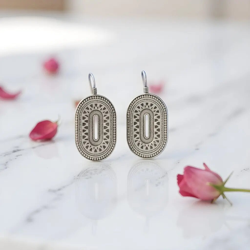 Silver Berber earrings with geometric oval design and oxidized finish on marble surface with pink flowers