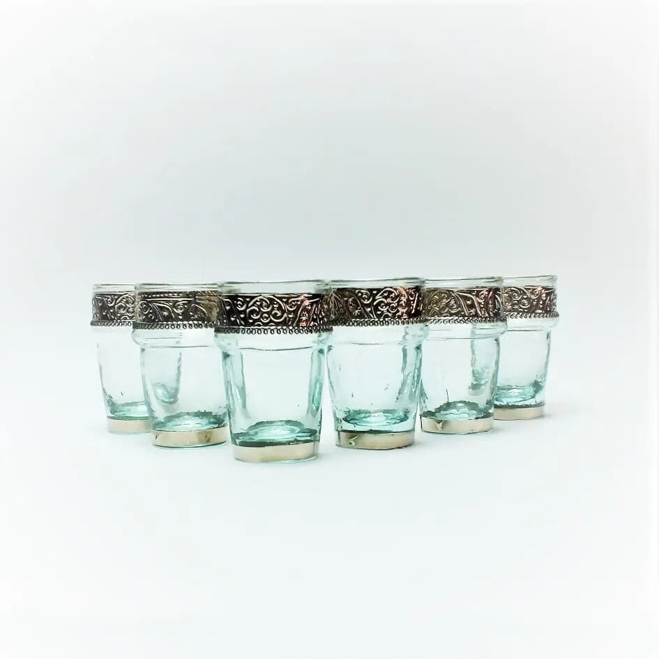 Six clear Moroccan tea glasses with silver filigree metal holders arranged in arc on white Six clear Moroccan tea glasses with silver filigree metal holders arranged in arc on white