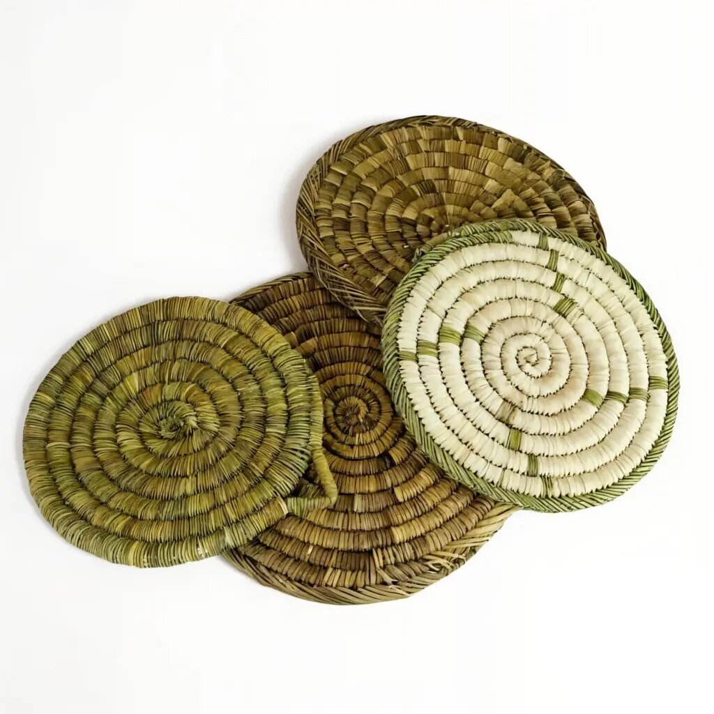 Hand-woven straw kitchenware placemats set in natural green and tan tones showing artisan spiral coil craftsmanship