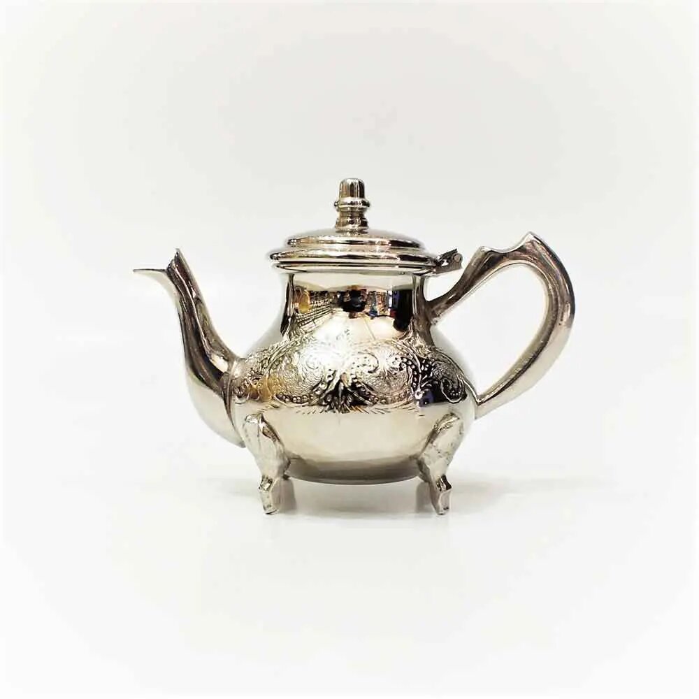 Floral engraved silver teapot with domed lid, curved spout, loop handle, and four ornate feet on a plain light backgroun Floral engraved silver teapot with domed lid, curved spout, loop handle, and four ornate feet on a plain light background