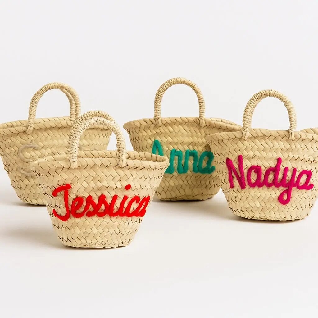Three mini straw bags with embroidered names Jessica Anna and Nadiya in red green and pink on natural palm leaf