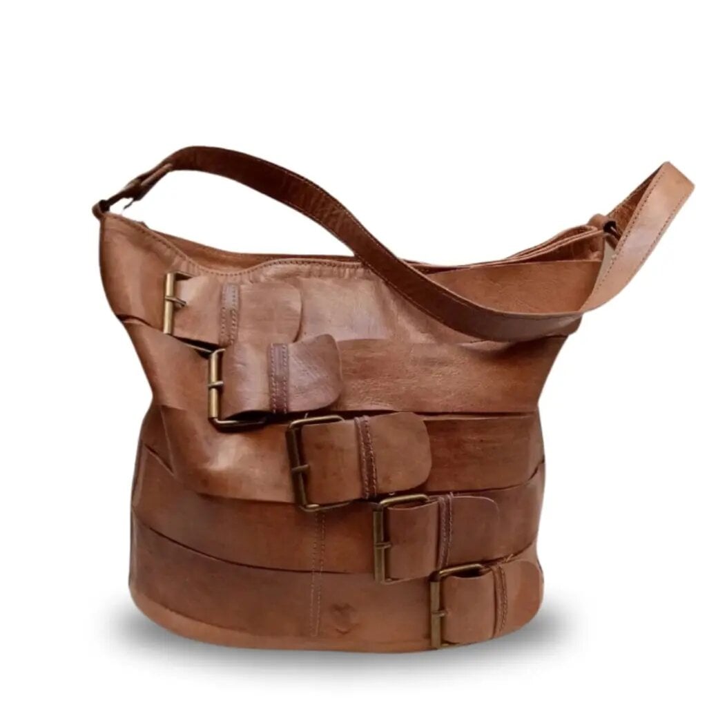 Sahara tan leather bucket tote bag with five decorative buckle straps and metal hardware on white background Sahara tan leather bucket tote bag with five decorative buckle straps and metal hardware on white background