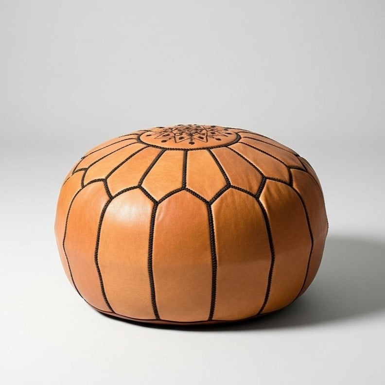 Handstitched light brown leather round ottoman with geometric embroidery on neutral studio background Handstitched light brown leather round ottoman with geometric embroidery on neutral studio background