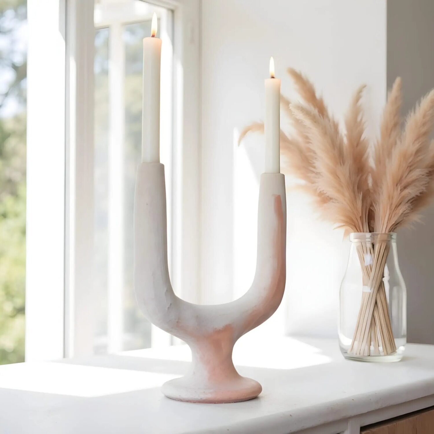 Handcrafted ceramic candle holder in white with twin arc design on windowsill with pampas grass decor