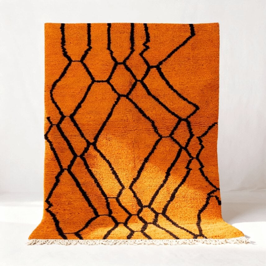 Orange geometric Moroccan rug with bold black diamond lattice pattern and white fringe displayed in full view