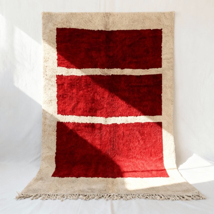 Red handwoven grid Moroccan rug with cream horizontal stripes and minimalist geometric pattern, propped on white
