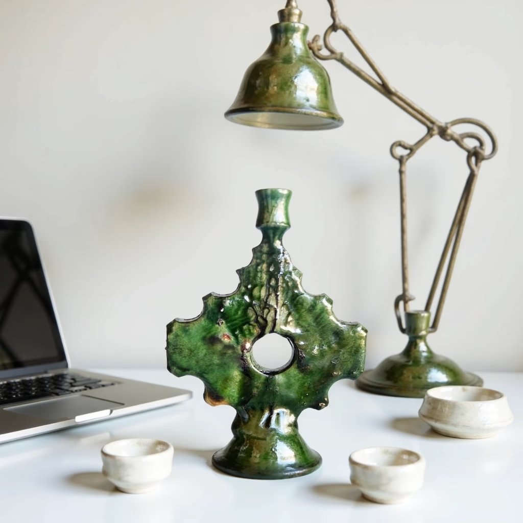 Vintage ceramic candle holder with emerald green Tamegroute glaze and ornate cross design on desk Vintage ceramic candle holder with emerald green Tamegroute glaze and ornate cross design on desk