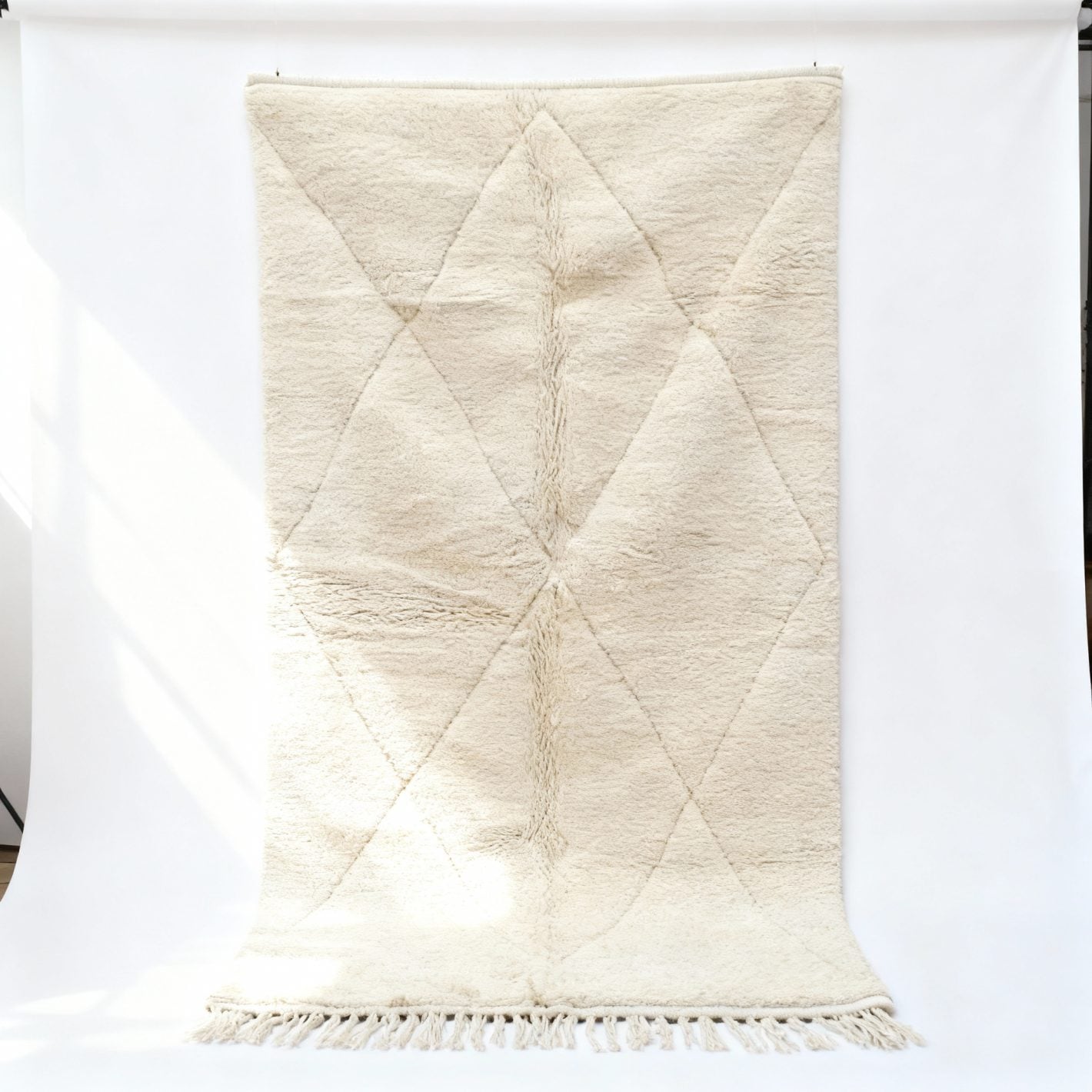 Handmade white Moroccan wool rug with Beni Ourain diamond pattern hanging on studio backdrop