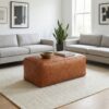 Light brown woven leather bench ottoman centered between grey sofas in modern living room Light brown woven leather bench ottoman centered between grey sofas in modern living room