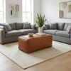 Woven leather bench ottoman on white rug in bright contemporary living room with grey sofas Woven leather bench ottoman on white rug in bright contemporary living room with grey sofas