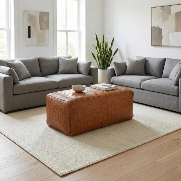 Woven leather bench ottoman on white rug in bright contemporary living room with grey sofas Woven leather bench ottoman on white rug in bright contemporary living room with grey sofas