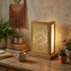 Single brass lantern table lamp on wooden desk in bohemian home office with plants and macrame wall hanging Single brass lantern table lamp on wooden desk in bohemian home office with plants and macrame wall hanging