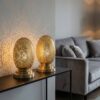 Two brass oval table lamps on modern console table casting decorative shadows in contemporary living space