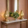 Two brass pear table lamps on marble console table with flowers casting decorative shadow patterns on pink wall Two brass pear table lamps on marble console table with flowers casting decorative shadow patterns on pink wall