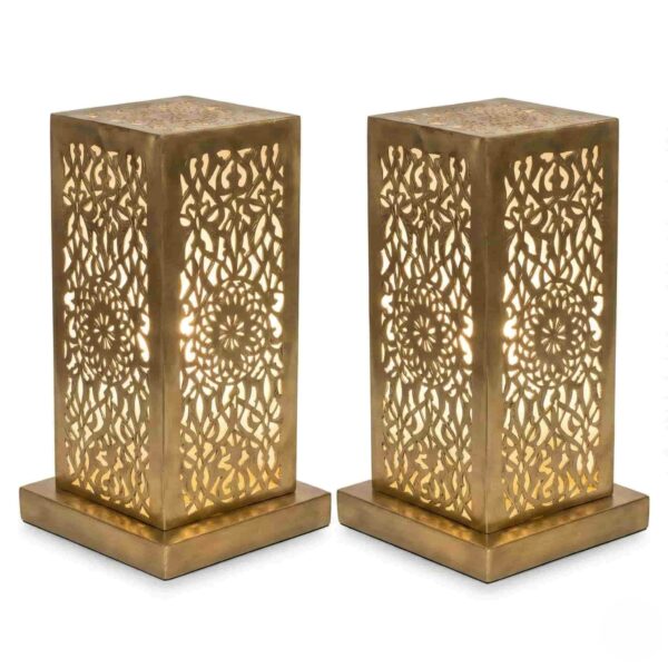 Pair of hand-engraved perforated brass table lamps with geometric floral patterns glowing warmly against white backgroun Pair of hand-engraved perforated brass table lamps with geometric floral patterns glowing warmly against white background
